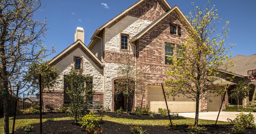 Exterior facade of two-story brick and stone home in residential neighborhood. Landscaped front yard, three-car garage.