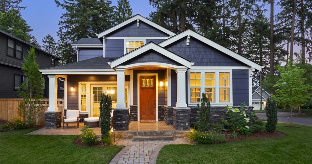 Facade of home with manicured lawn, landscaping, and backdrop of trees and dark blue sky. Glowing interior lights create a welcoming mood.