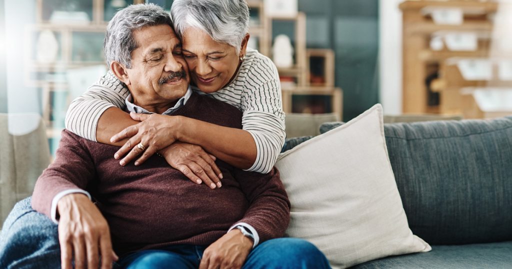 cheerful elderly woman hugging her husband who's in a wheelchair at home during the day